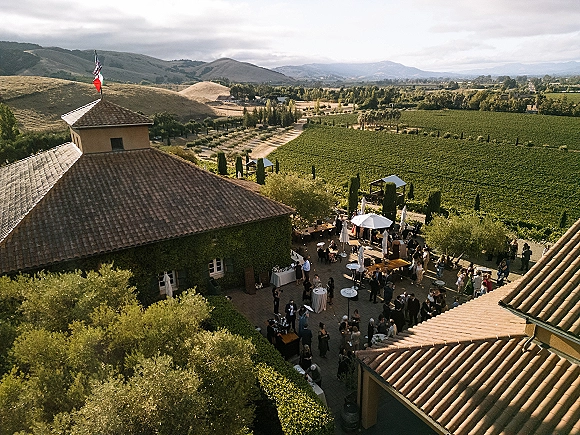 Outdoor wedding reception in a vineyard wedding reception courtyard with cocktail tables, patio umbrellas, string lights, and mountain views