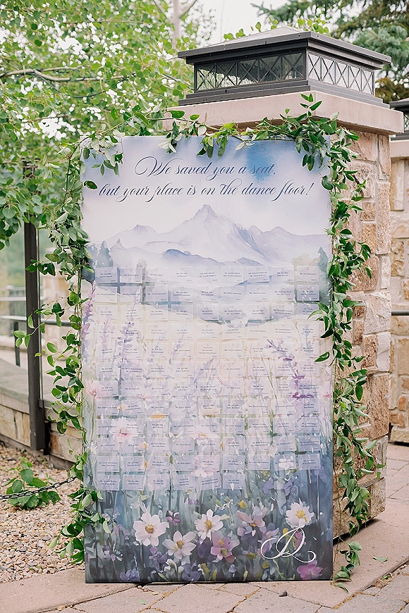 Wedding seating chart with escort card display, calligraphy sign framed by greenery garland on a patio by stone pillars and lanterns