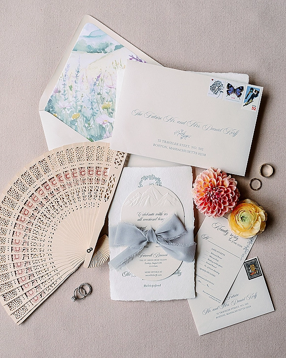 Invitation suite wedding invitation flat lay with deckle edge cards, watercolor liner, blue silk ribbon, stamps and rings on linen fabric