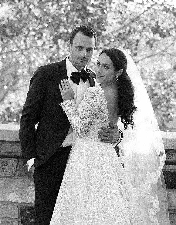 Couple portrait in black and white wedding portrait style, bride in lace long sleeves and cathedral veil embracing groom in tux on stone terrace