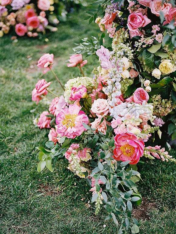 Wedding floral arrangement with pink roses and peonies, hydrangea and greenery foliage set on a grass lawn in a garden