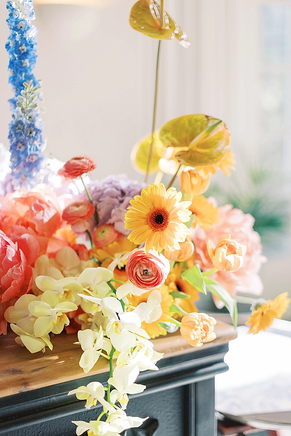 Wedding floral arrangement colorful wedding centerpiece of orchids, ranunculus, gerbera daisies, anthurium and greenery on a wooden table by window light