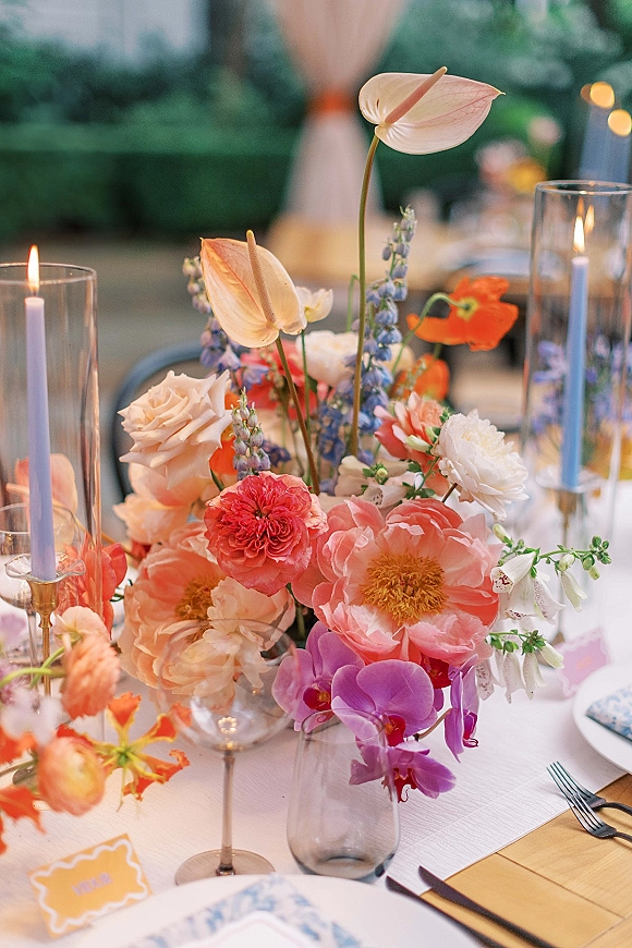 Wedding centerpiece with colorful wedding centerpiece flowers, taper candles and glass hurricane on a banquet table under bistro lights outdoors