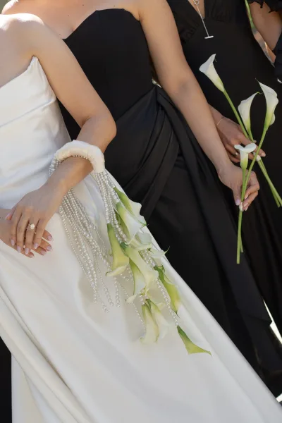 Calla lily bouquet styled as a cascading bouquet with delicate pearl strands, set against white gown fabric and black dress fabric.