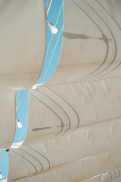 Tent ceiling decor with wedding tent lighting and string lights woven through white draping and poles, open to a blue sky
