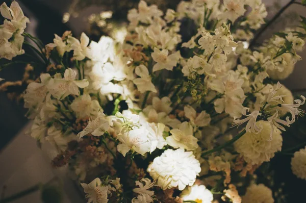 Wedding centerpieces with white wedding centerpiece blooms and greenery arranged on a table setting in dim reception lighting
