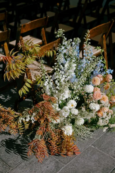 Ceremony aisle flowers create a wildflower meadow along a stone patio aisle, with greenery accents and wooden chairs in rows