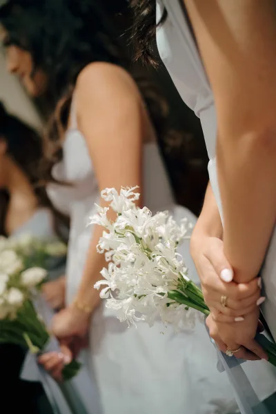 Bridesmaids portrait of hands holding white wedding bouquets, showing manicured nails and rings against soft indoor bokeh light