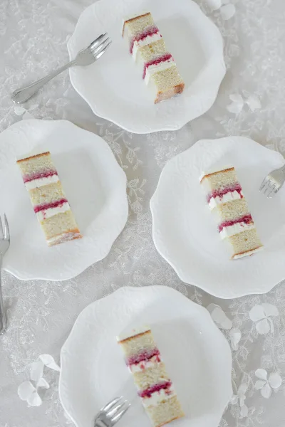 Wedding cake slices on white plates with forks, set on a lace tablecloth for wedding cake serving with scattered white flower petals