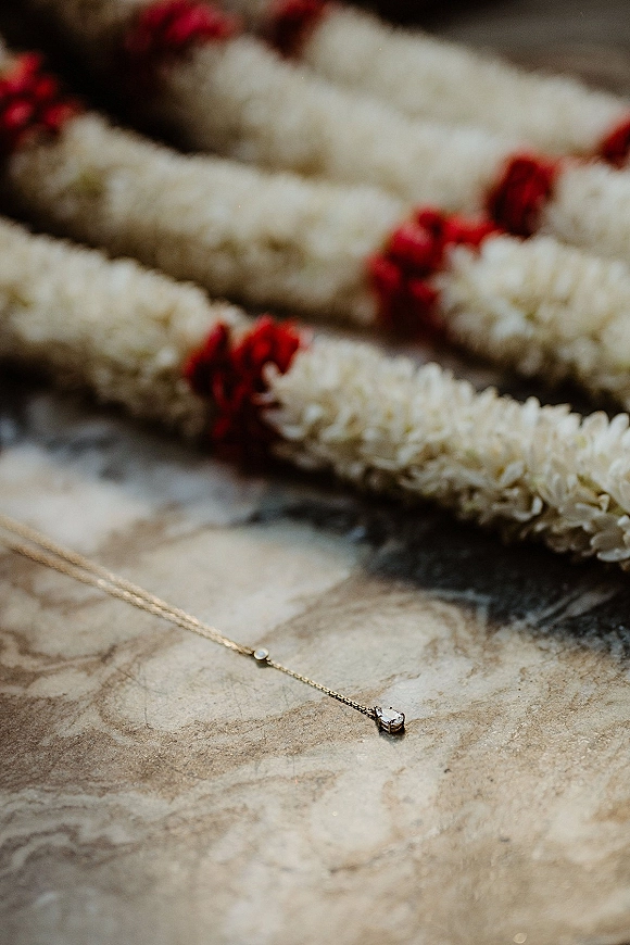 Wedding necklace with bridal necklace gold pendant and gemstone on marble, framed by red flower garlands for a romantic flat lay detail