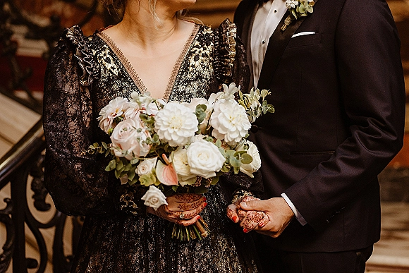 Couple portrait of bride and groom holding hands, her white rose bouquet with eucalyptus and henna nails by a warm ornate staircase