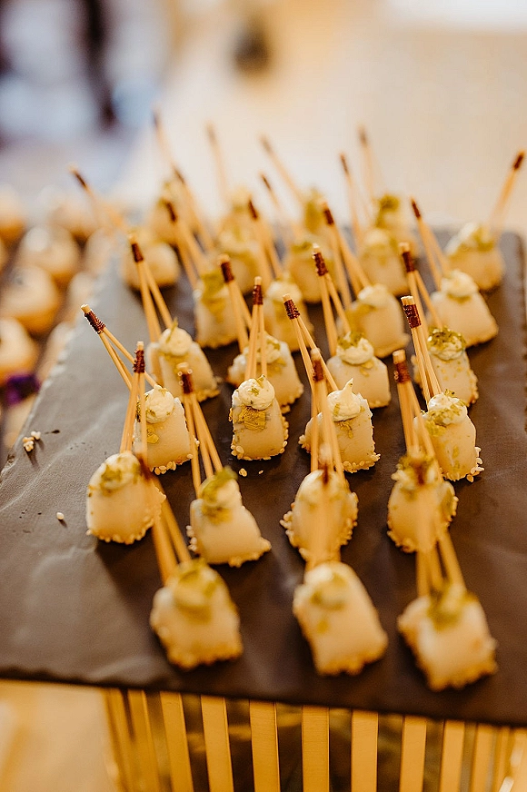 Wedding appetizers with cocktail hour appetizers on skewers, creamy-topped bites arranged on a slate platter at a buffet table indoors
