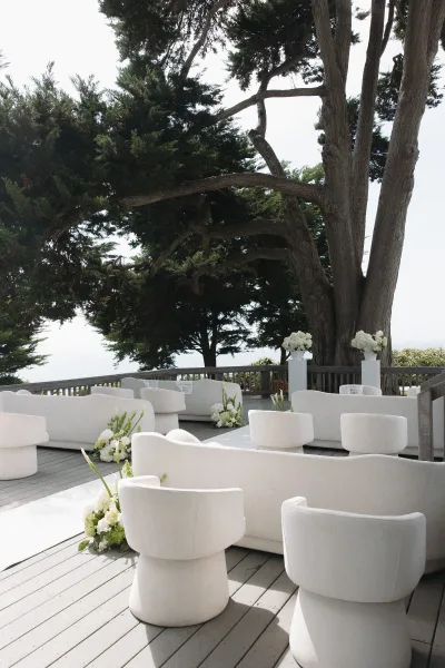 Wedding lounge setup for an outdoor reception lounge with sofas on a wood deck beneath large trees overlooking the ocean.