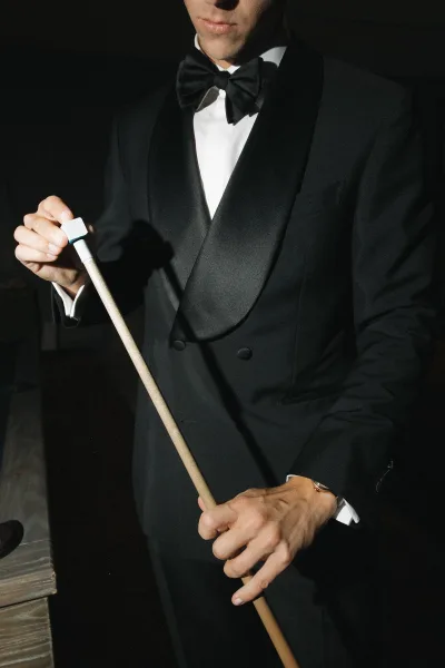 Groom portrait of a black tie groom aiming a pool cue over a billiards table in a moody dark room with wood surfaces
