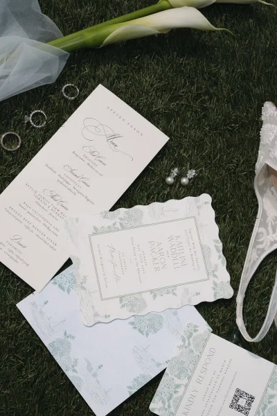 Invitation suite neatly styled as a wedding invitation flatlay on a grass lawn, accented with calla lilies.