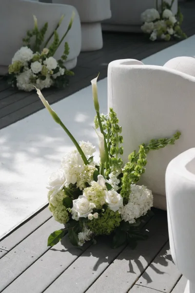 Ceremony aisle flowers arranged as grounded aisle florals with white roses lining the aisle on a wood deck.
