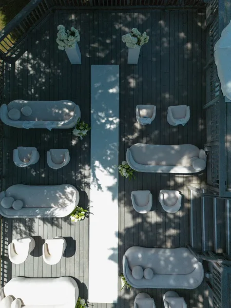 Ceremony setup featuring a lounge seating ceremony arranged on a wooden deck with railings and dappled tree shadows.
