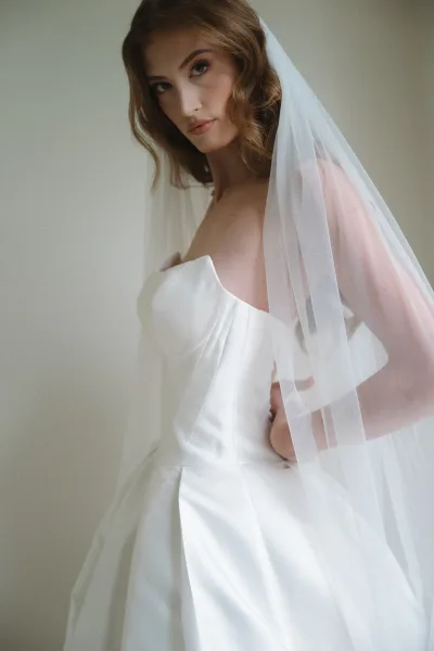 Bridal portrait of a bride with veil, posed in soft natural light, minimalist style with loose waves and an elegant, timeless expression.
