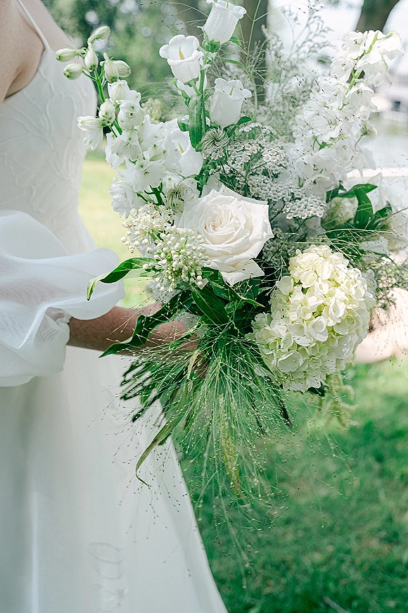 Bridal bouquet of white roses, calla lilies, hydrangea and lily of the valley with greenery accent, held against a garden lawn background
