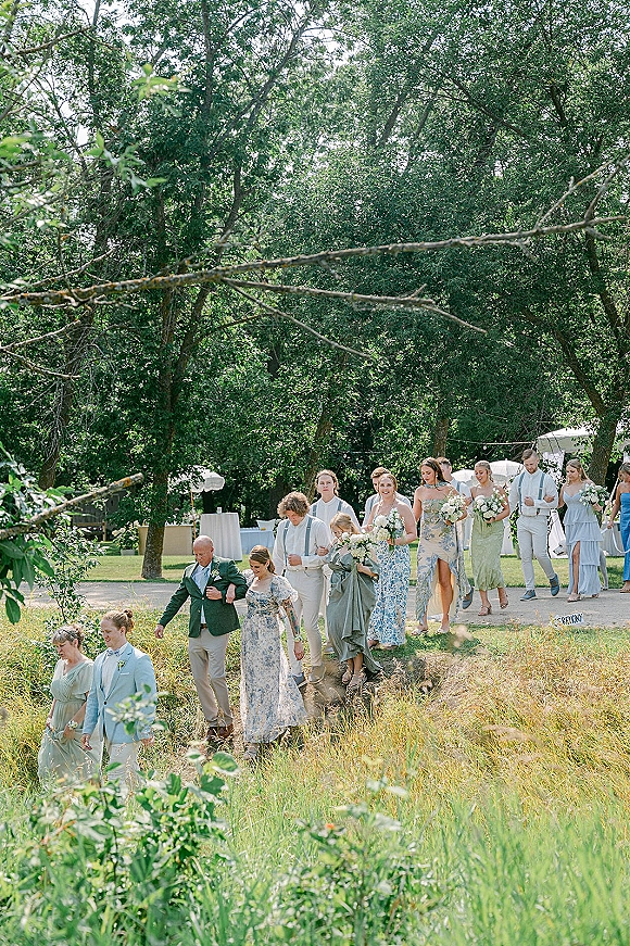 Wedding processional with outdoor wedding processional bridal party walking a dirt path in a grassy field, groomsmen in suspenders and parasols