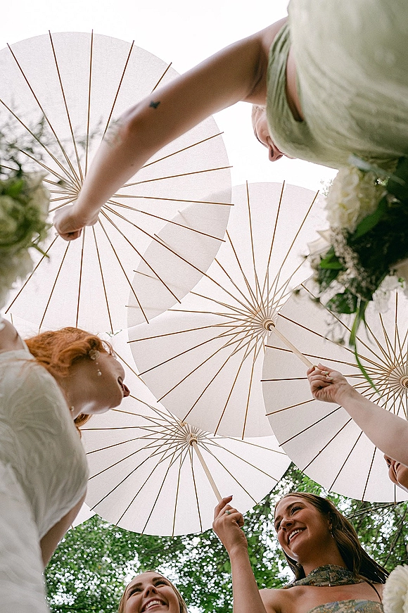 Bridesmaids portraits with bridesmaids holding parasols, looking down in a circle with bouquets and earrings against trees and sky