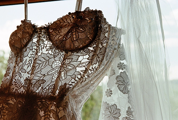 Wedding dress with lace wedding dress bodice, floral embroidery and illusion neckline on a hanger in window light with greenery beyond