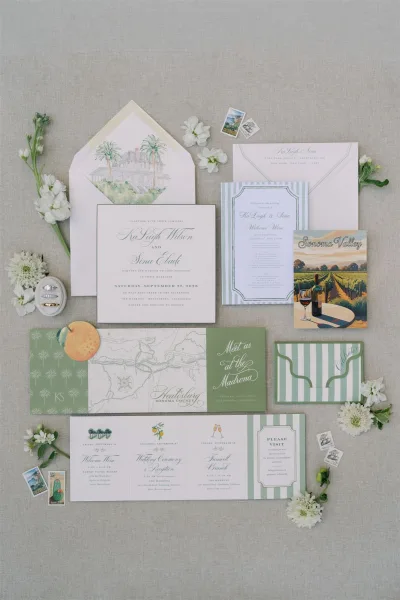 Invitation suite wedding invitation flat lay with watercolor venue illustration, RSVP and map cards, rings, and white flowers on linen backdrop