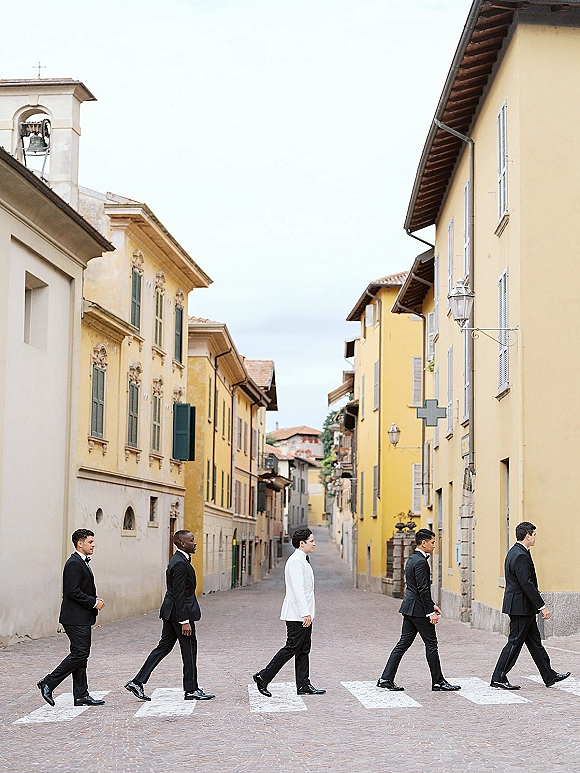 Groomsmen portrait of a wedding party walking in black tie, groom in a white dinner jacket on a cobblestone crosswalk downtown