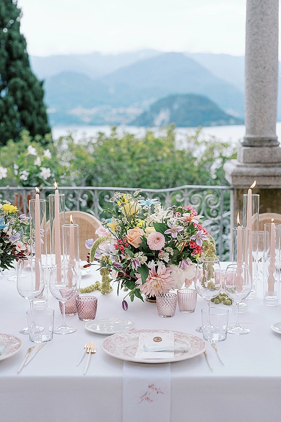 Reception tablescape with pastel wedding centerpiece, taper candles and pink votives on a terrace balcony overlooking lake and mountains