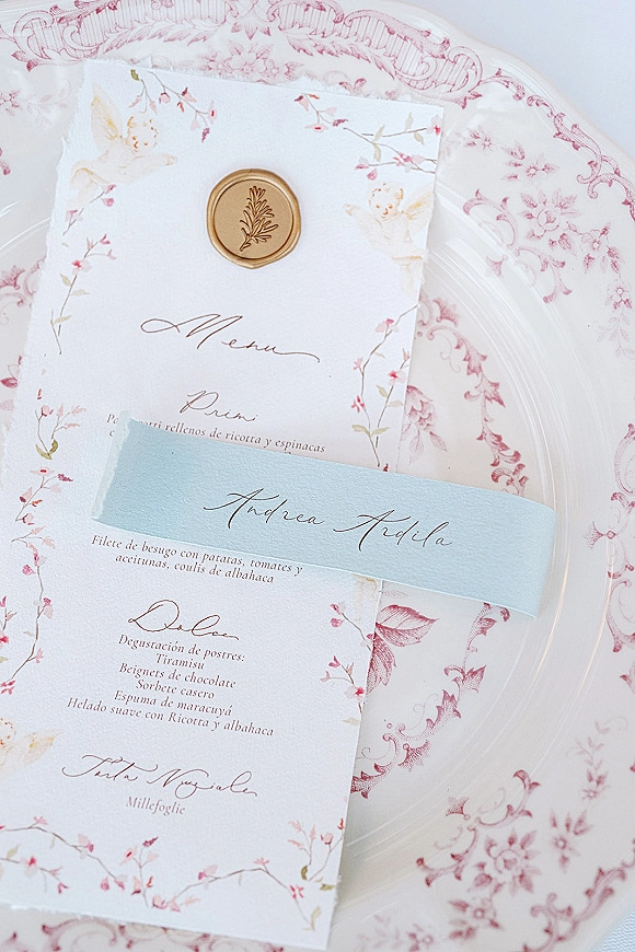 Wedding menu card with calligraphy wedding menu lettering, blue belly band and gold wax seal on charger plate over patterned linens