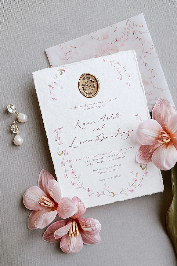 Wedding invitation suite with deckle edge wedding invitation, calligraphy, monogram wax seal, floral liner, and pink flowers on linen flat lay