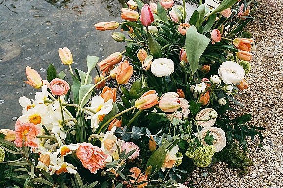 Wedding florals with spring wedding flowers, featuring tulips and ranunculus nestled in moss and greenery along a gravel path by water