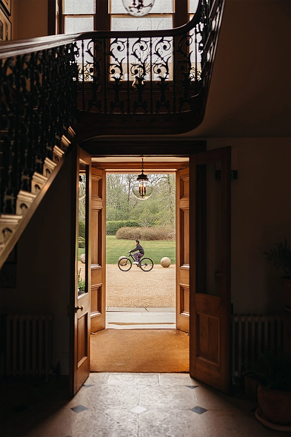 Wedding venue entrance with open double doors framing a garden view, pendant globe light overhead and wrought iron staircase railing beside stone tile floor