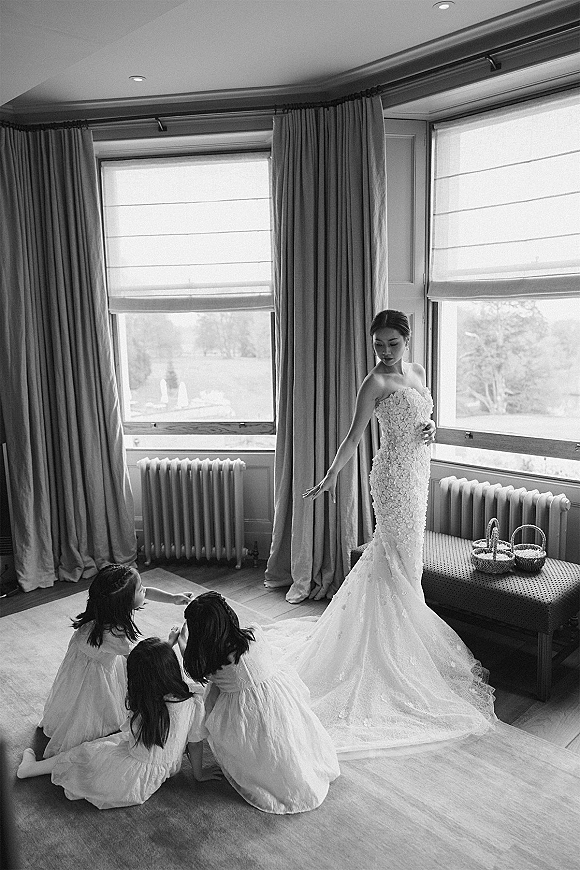 Bride portrait in a strapless lace wedding dress with cathedral train, looking down by large windows in a softly lit room