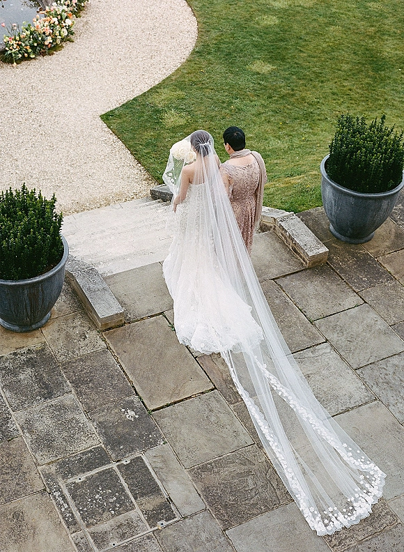 Bride and mother share a moment as mother helping bride adjust a cathedral length veil train on stone terrace steps with topiary accents
