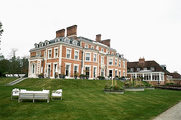 Wedding venue exterior with estate wedding venue terrace, white patio umbrellas, lounge seating, and fountain in front of a brick manor house