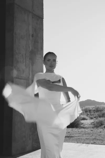 Bridal portrait of a modern bride in a minimalist gown, posed against a concrete wall with desert mountains and open sky in the distance.