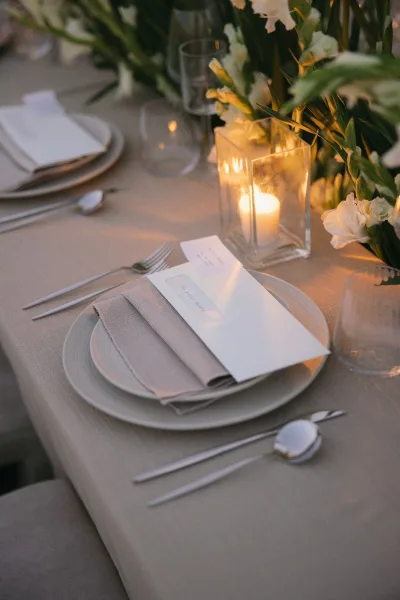 Wedding place setting at a candlelit reception table with a menu card, styled in a neutral palette on taupe table linens