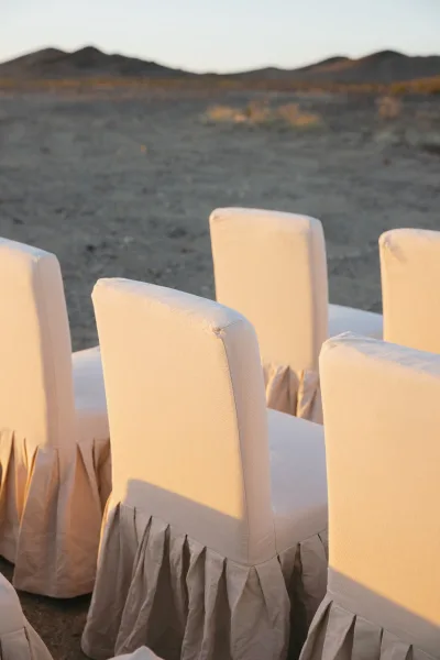 Ceremony seating with wedding chair covers detailed with pleated skirts, set on gravel against a desert landscape with distant mountains.