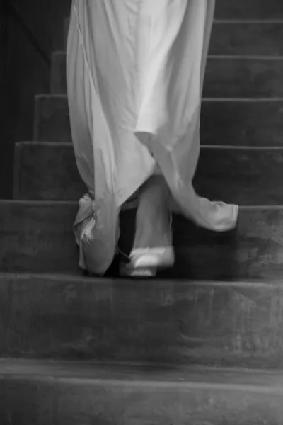 Bride on stairs walking in wedding dress reveals platform heels as she ascends an indoor concrete stairway in a candid, elegant moment.
