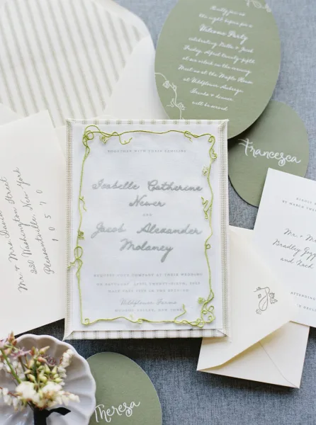 Wedding invitation suite with embroidered wedding invitation, calligraphy cards and envelopes arranged on linen with a floral sprig accent
