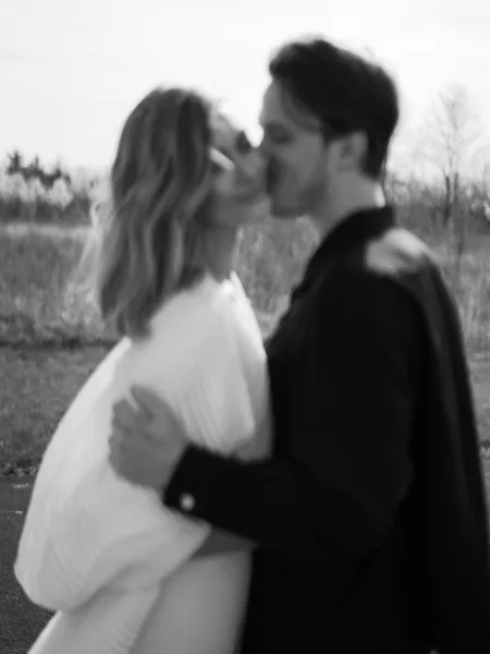 Wedding kiss as bride in long-sleeved gown and groom in dark suit embrace in a tall grass field under open sky