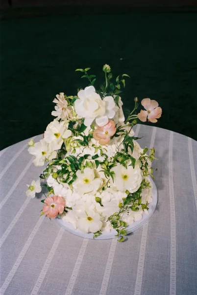 Wedding cake with white buttercream frosting and fresh flower topper on a cake stand over a striped tablecloth against a dark backdrop