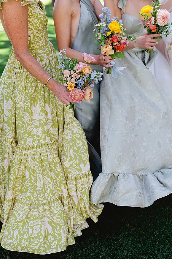 Bridesmaid bouquets in wildflower bridesmaid bouquets style, hand-tied with ribbon wrap, held by bridesmaids on a green lawn outdoors