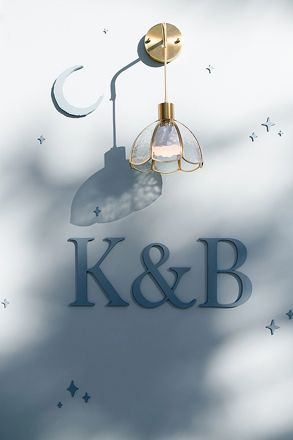 Wedding monogram sign with wedding initials wall sign in raised letters and ampersand, lit by brass sconce on a white wall with moon accent