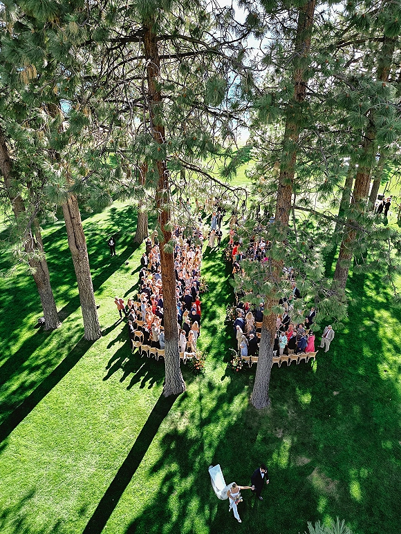 Outdoor wedding ceremony captured in an aerial wedding ceremony view, circular seating with aisle florals beneath pine trees and lawn shadows