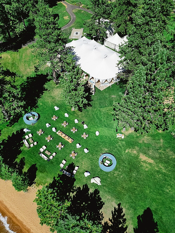 Outdoor reception setup with a wedding tent reception under a white sailcloth tent, cocktail tables and lounge seating on a lakeside lawn