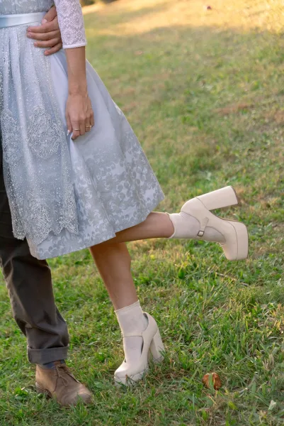 Bridal shoe detail with wedding platform heels and white ankle socks, bride leg pop pose beside groom on a sunlit grass lawn