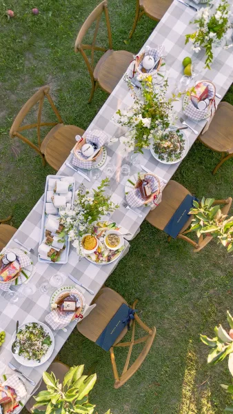Reception tablescape with outdoor reception table details, gingham runner, wildflower centerpieces, taper candles, and place settings on a garden lawn