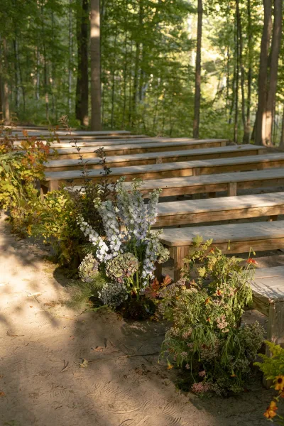 Ceremony seating with outdoor wedding benches lining a dirt aisle, with hydrangea and greenery florals in sunlit forest trees